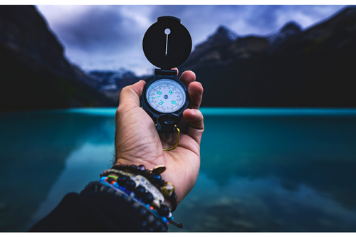 Left hand holding compass with calm lake behind